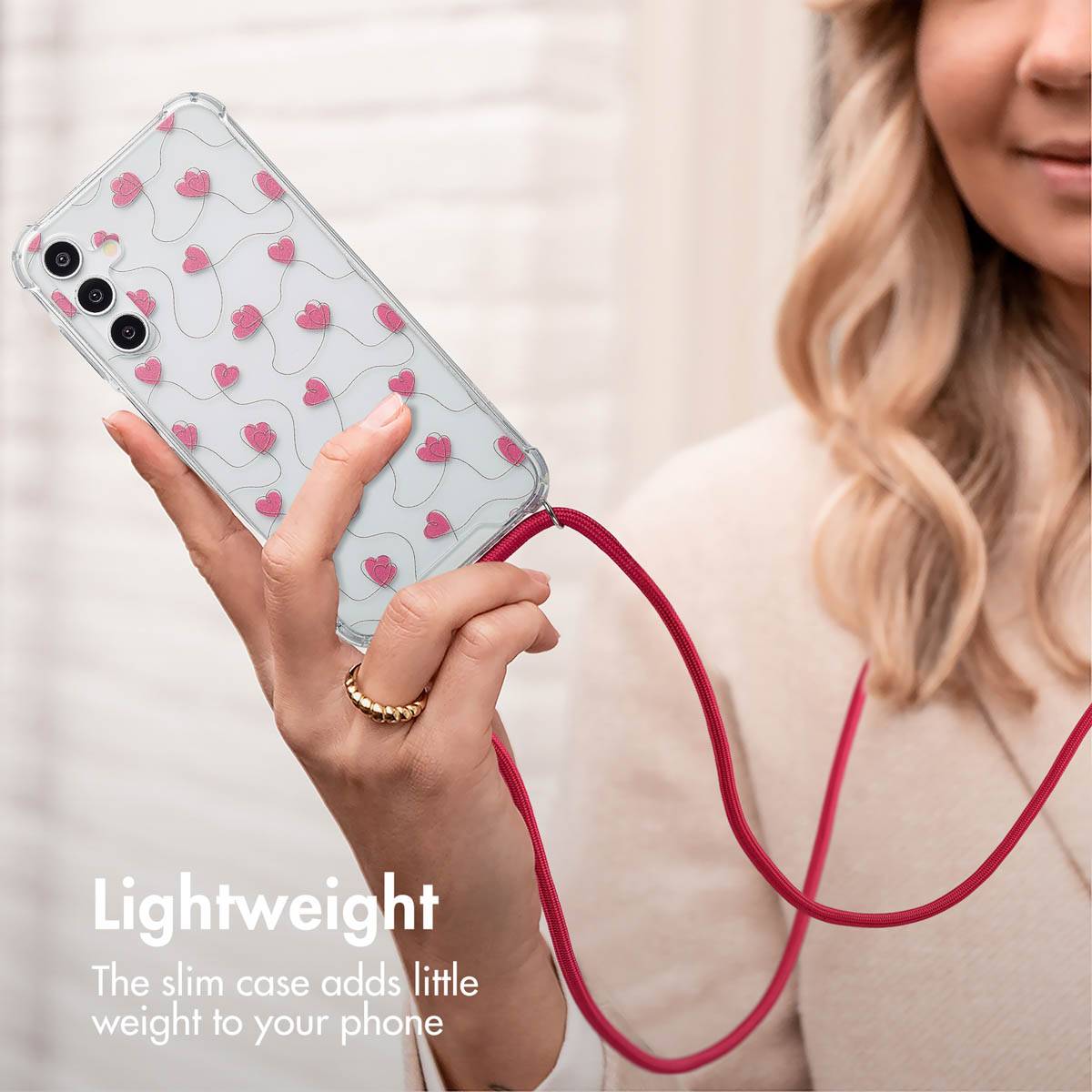 Una donna tiene uno smartphone con custodia trasparente, cuori rosa e laccetto rosso.
