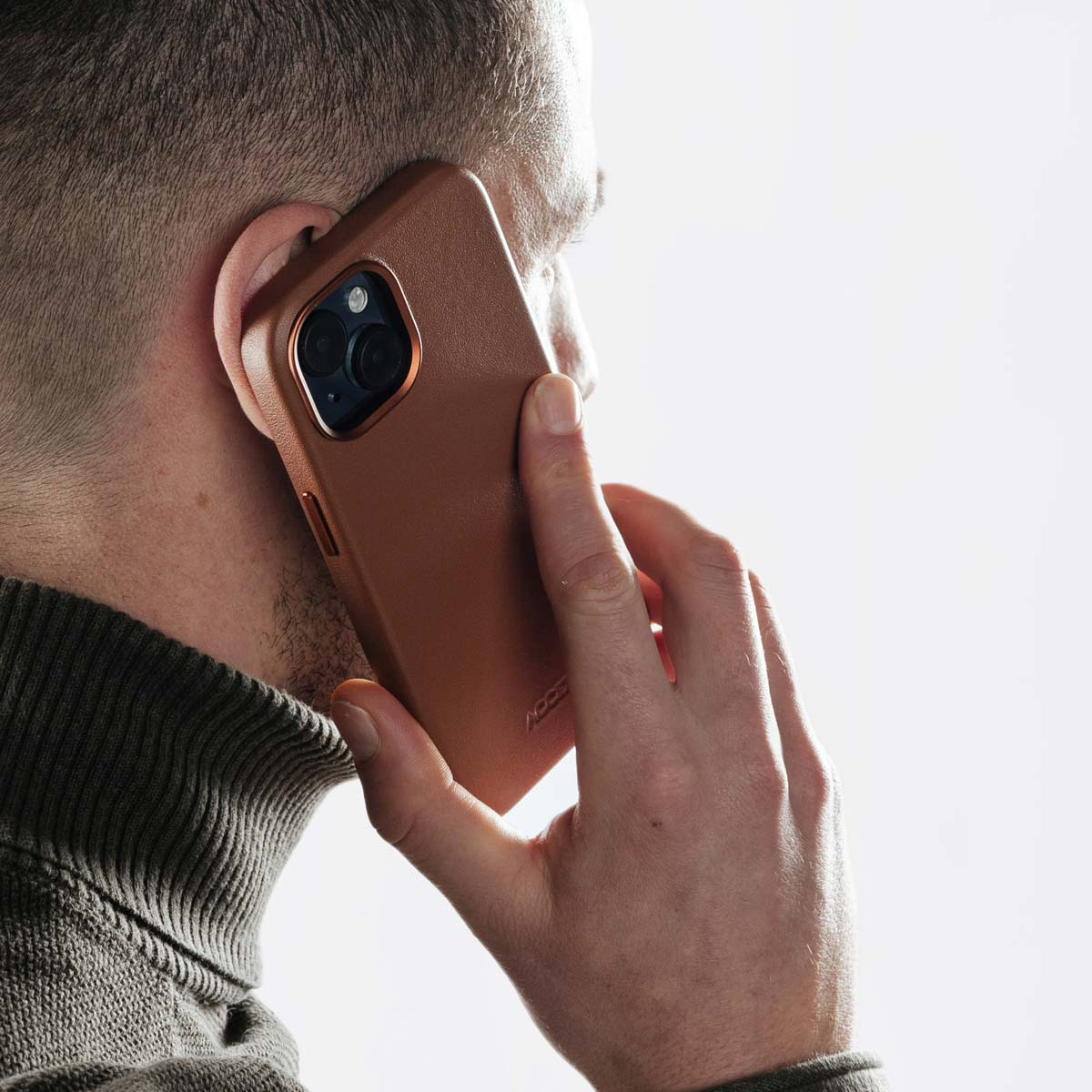 Un hombre hablando por un teléfono inteligente con funda de cuero marrón sobre fondo blanco.