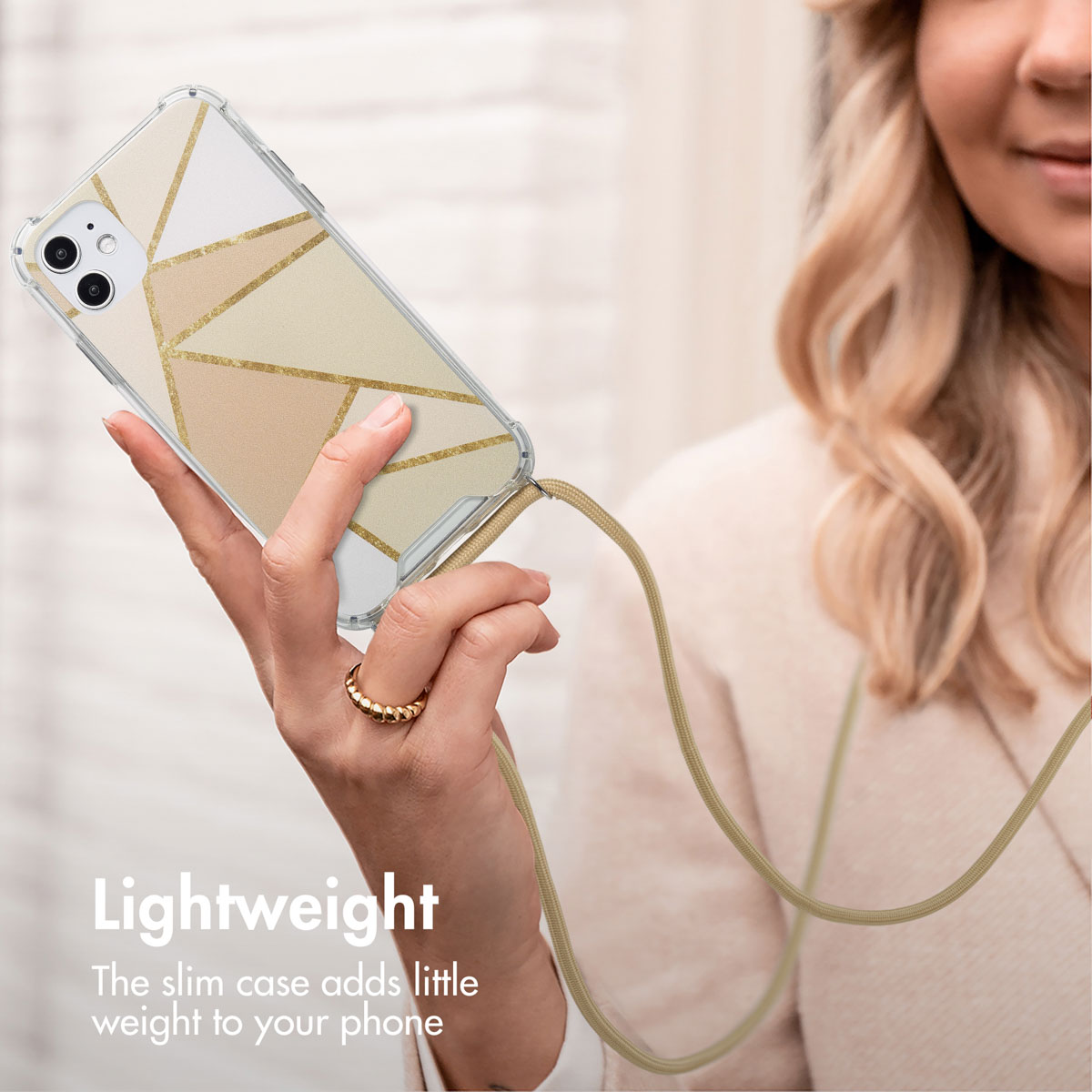 Une femme tient un smartphone avec une coque de protection à motif doré et une lanière assortie.