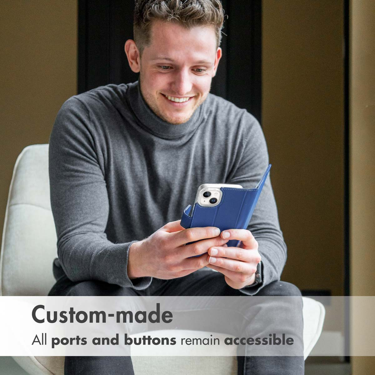 Un uomo siede su una poltrona, sorridendo mentre guarda il suo smartphone blu.