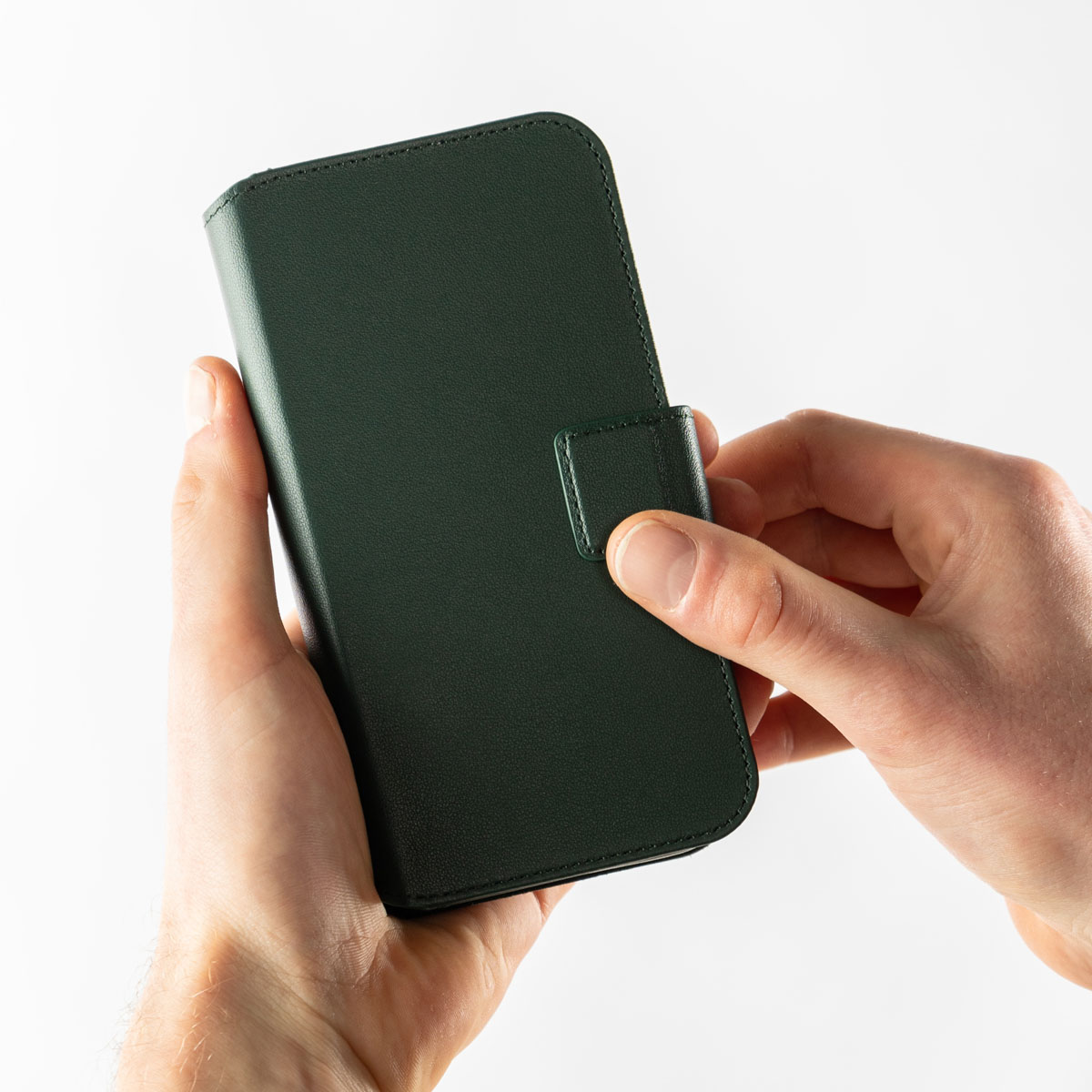 Des mains tenant un étui de téléphone en cuir vert foncé sur fond blanc.