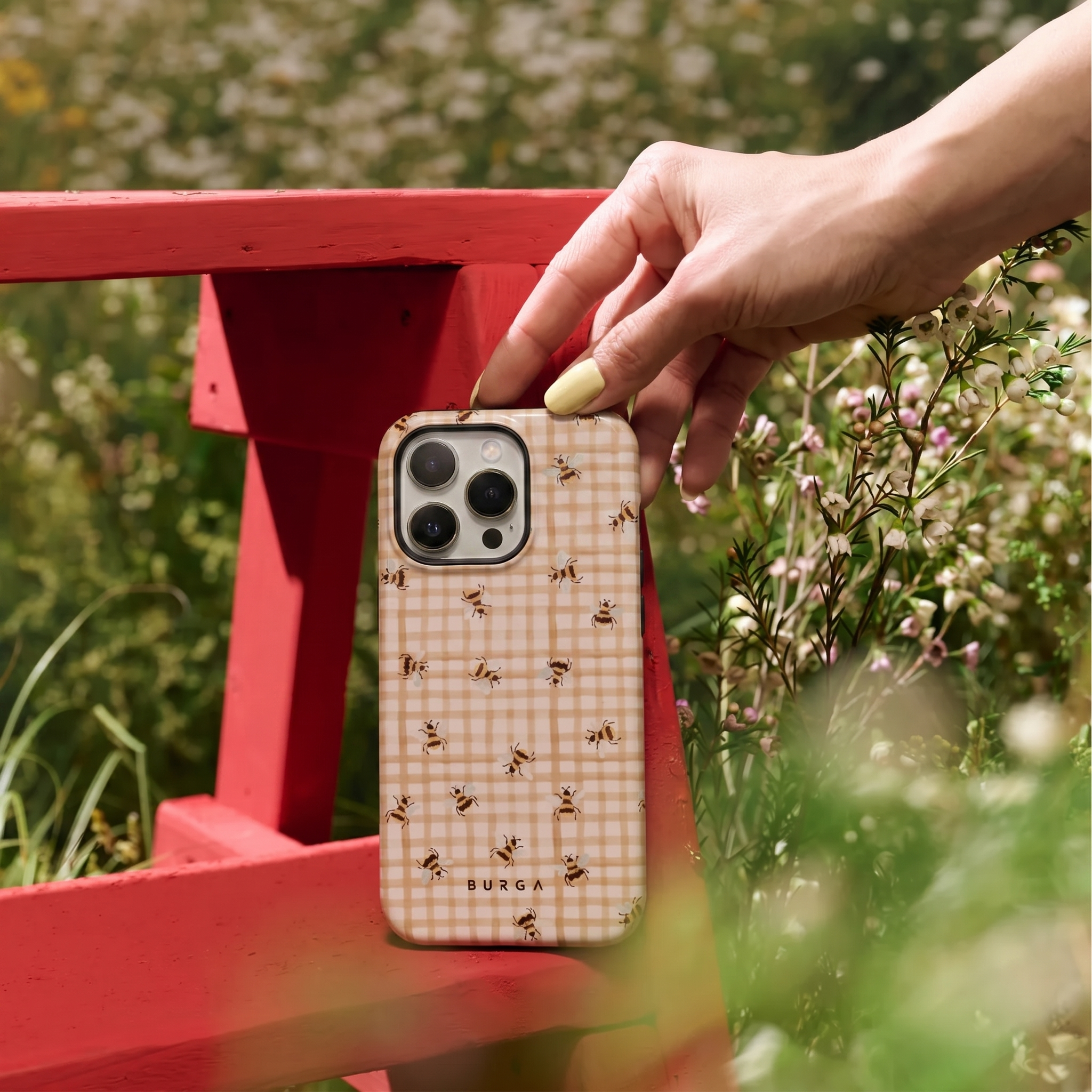Hand houdt een telefoonhoesje met bijenpatroon vast op een rode bank.