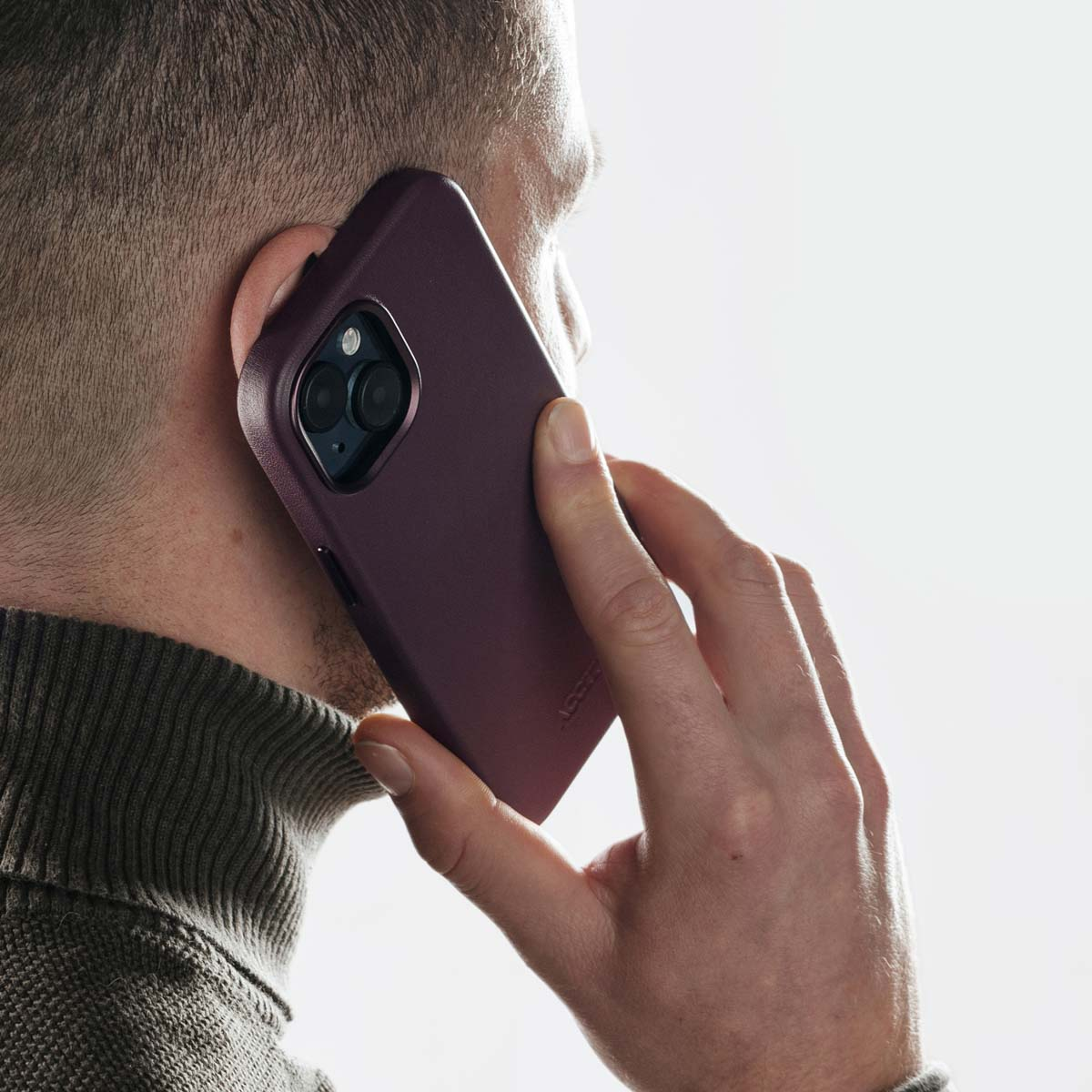 Un uomo parla al telefono con uno smartphone con custodia rosso scuro, tenendolo all'orecchio.
