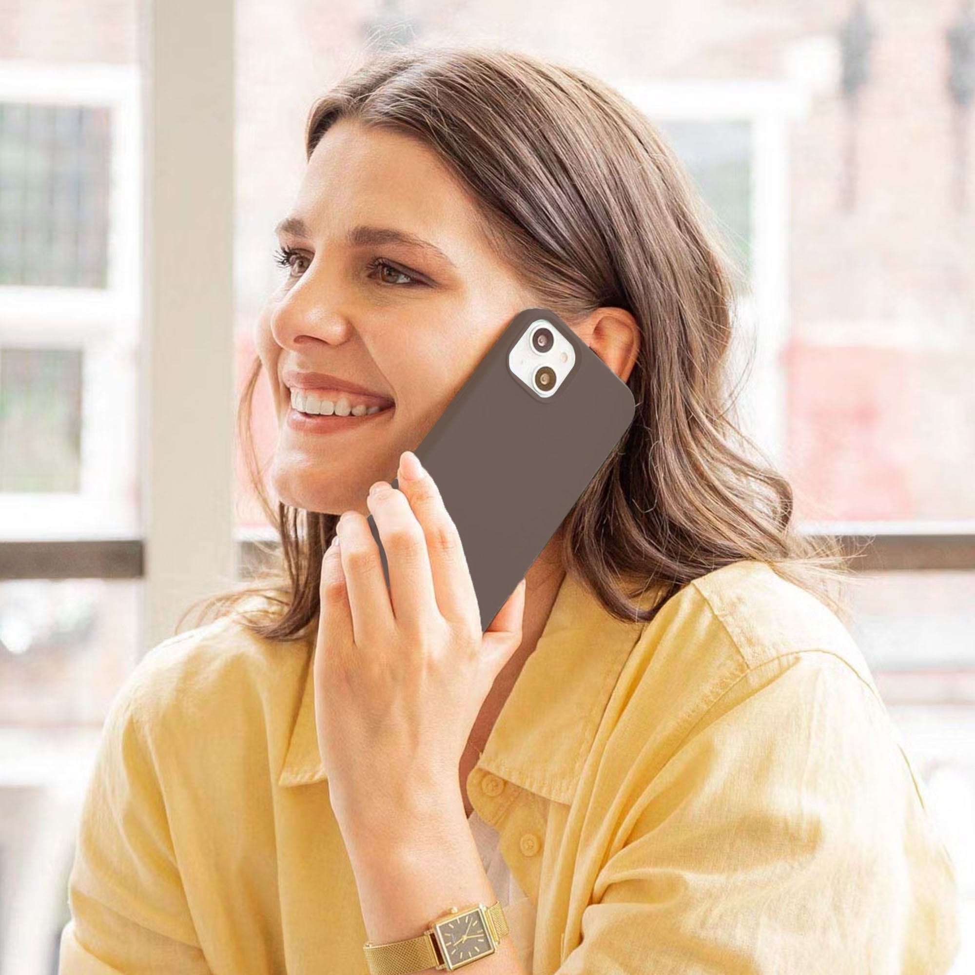 Een glimlachende vrouw in een geel shirt belt met een bruine smartphone.