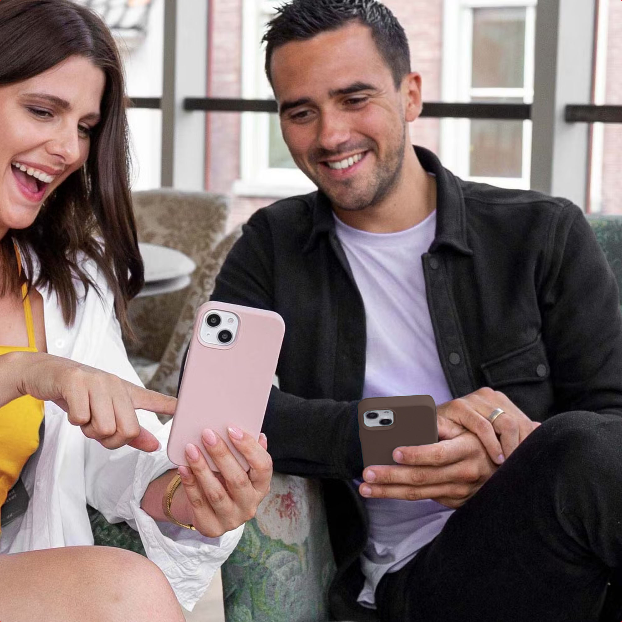 Een gelukkig stel kijkt naar hun smartphones, zij wijst naar haar roze scherm terwijl hij zijn bruine telefoon vasthoudt.