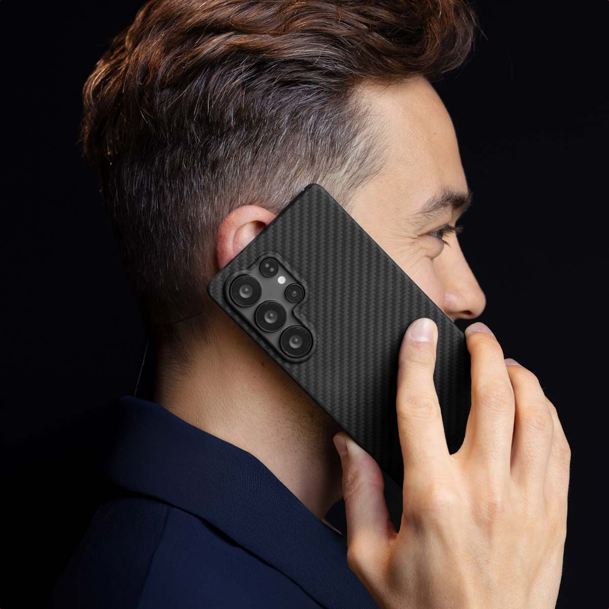 Un homme passe un appel sur un smartphone noir en carbone sur fond sombre.