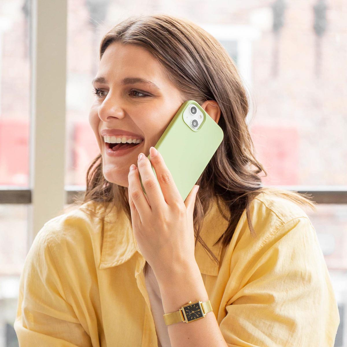 Una mujer sonriente con camisa amarilla habla por un smartphone verde claro.