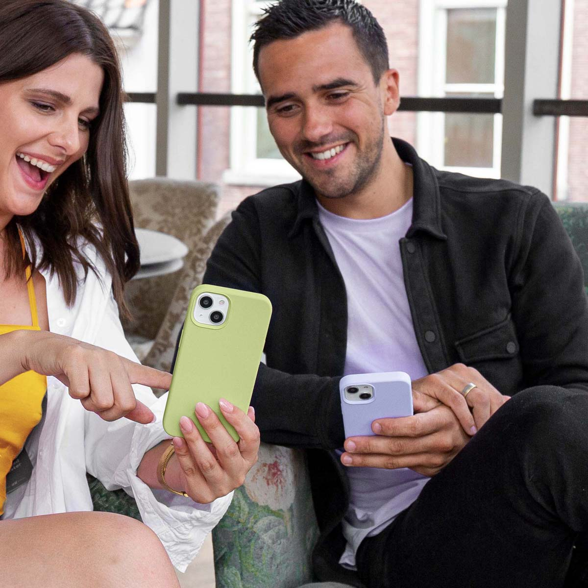 Una pareja feliz se sienta junta sosteniendo teléfonos inteligentes y sonriendo a una pantalla verde.