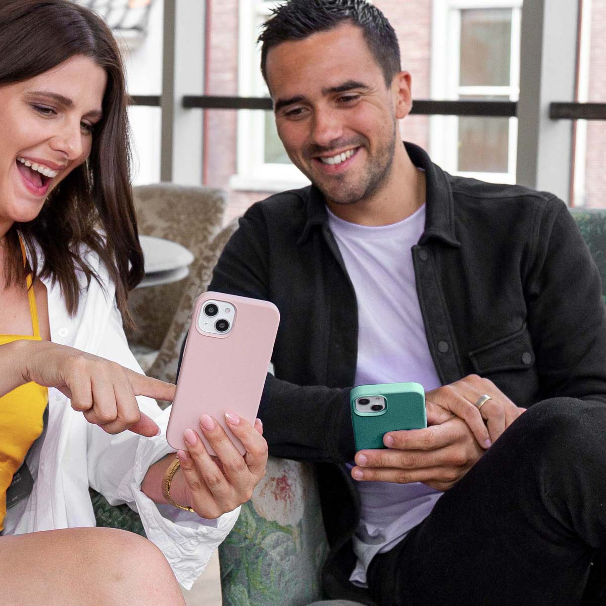 Un hombre y una mujer sonríen mientras miran sus teléfonos inteligentes en el interior.