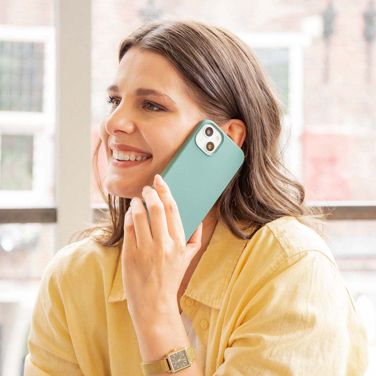 Una mujer sonriente con camisa amarilla habla por un smartphone verde menta.
