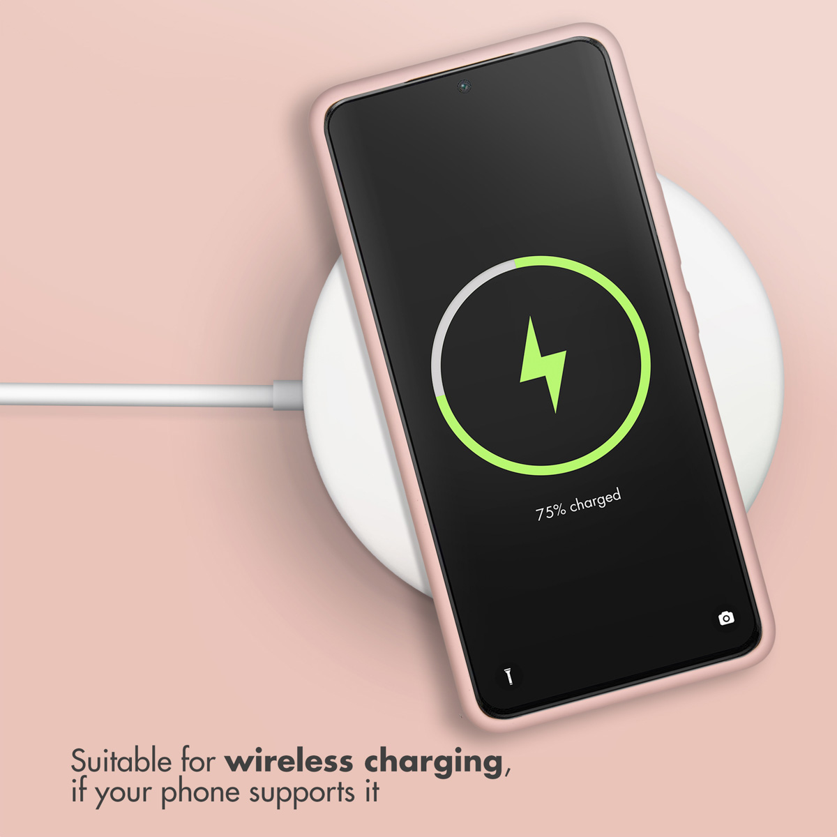 Un smartphone se charge sans fil sur un socle blanc sur fond rose.