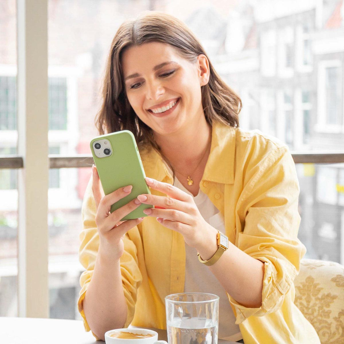 Una mujer sonriente con camisa amarilla está sentada en una mesa y escribe en su teléfono.