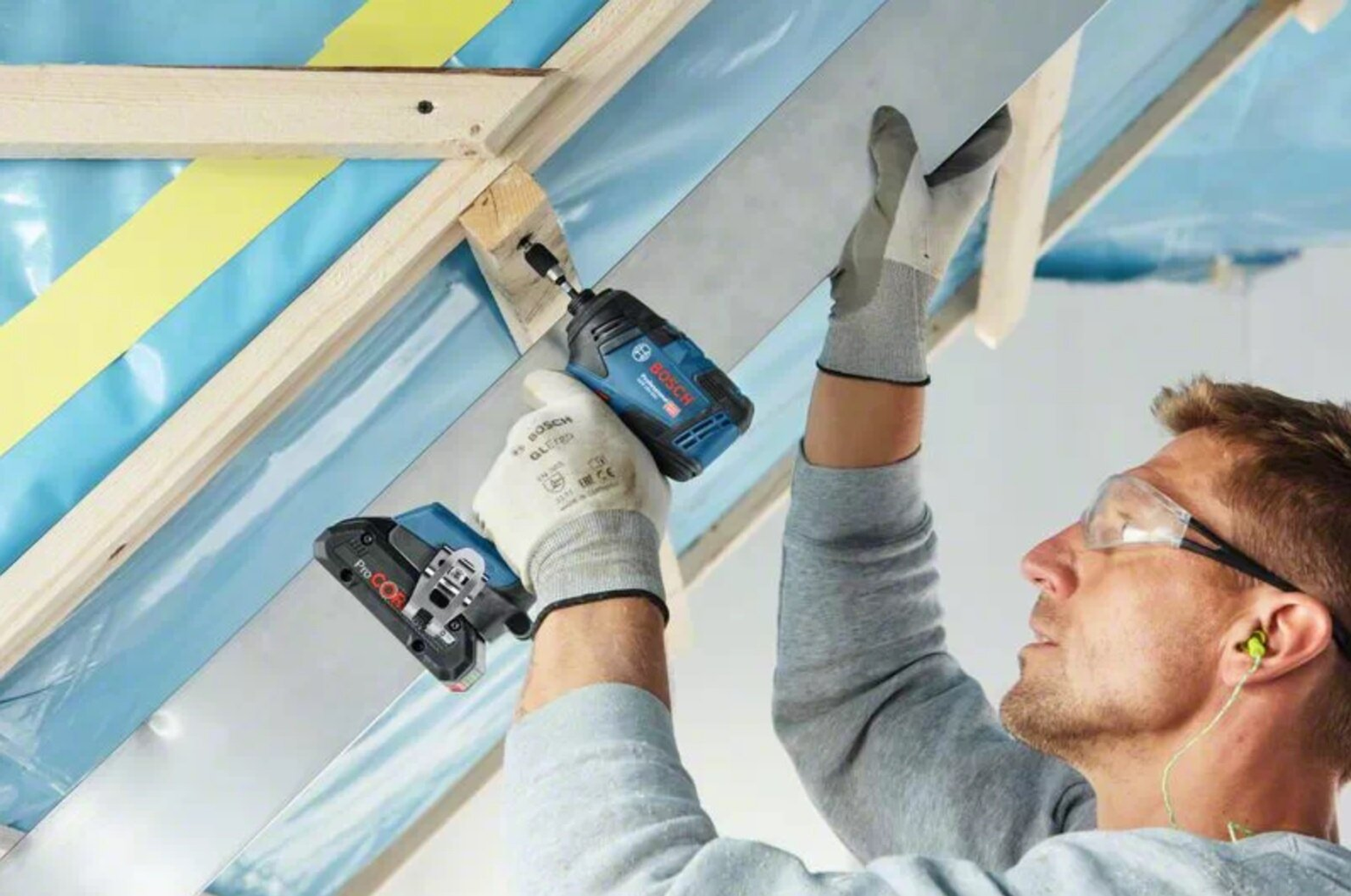 Ein Handwerker mit Schutzbrille schraubt mit einem Bosch-Akkuschrauber an einer Deckenkonstruktion.
