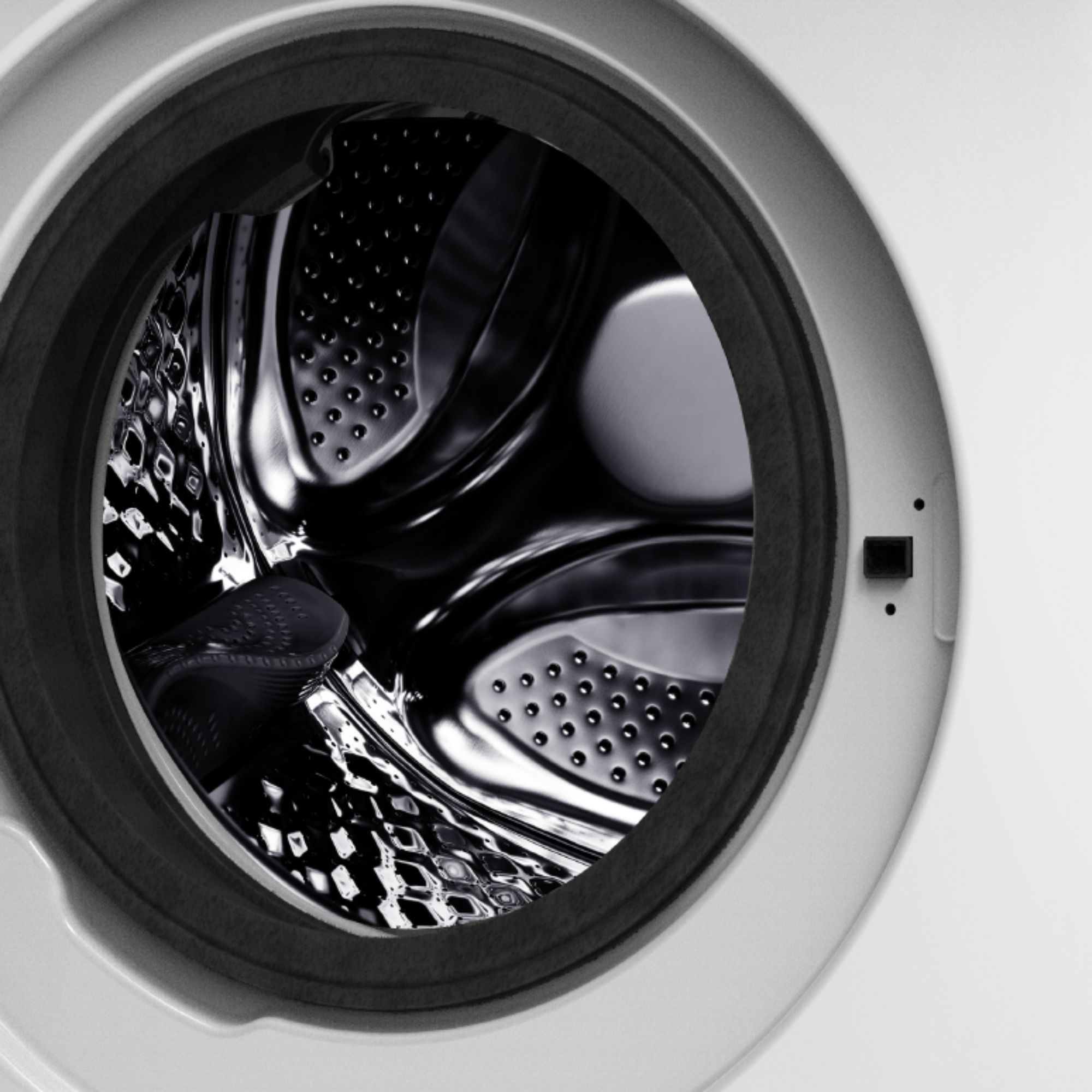 El interior del tambor de una lavadora vacía con superficie de acero inoxidable brillante y perforaciones.