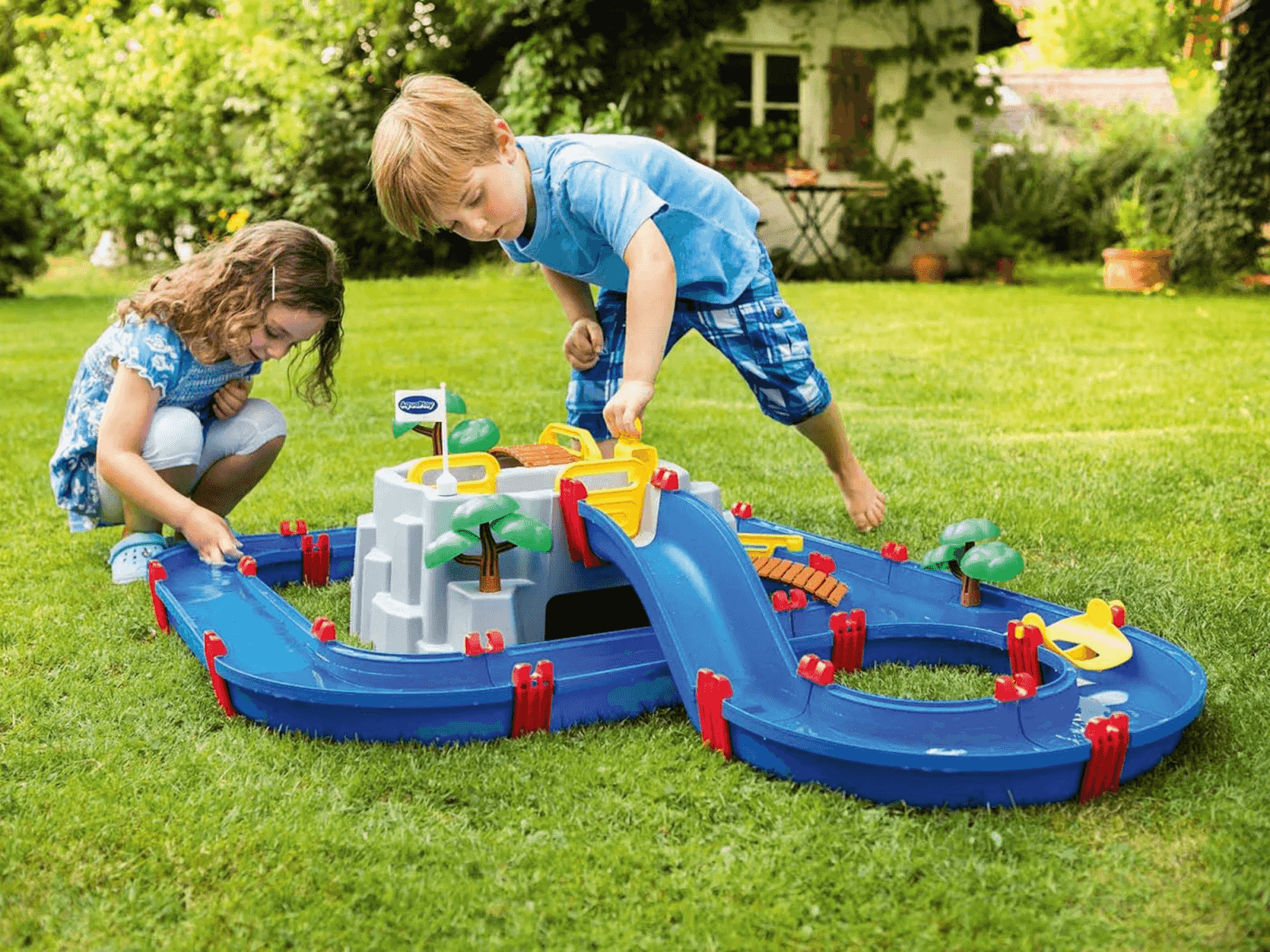 Due bambini che giocano all'aperto in giardino con un gioco d'acqua blu.