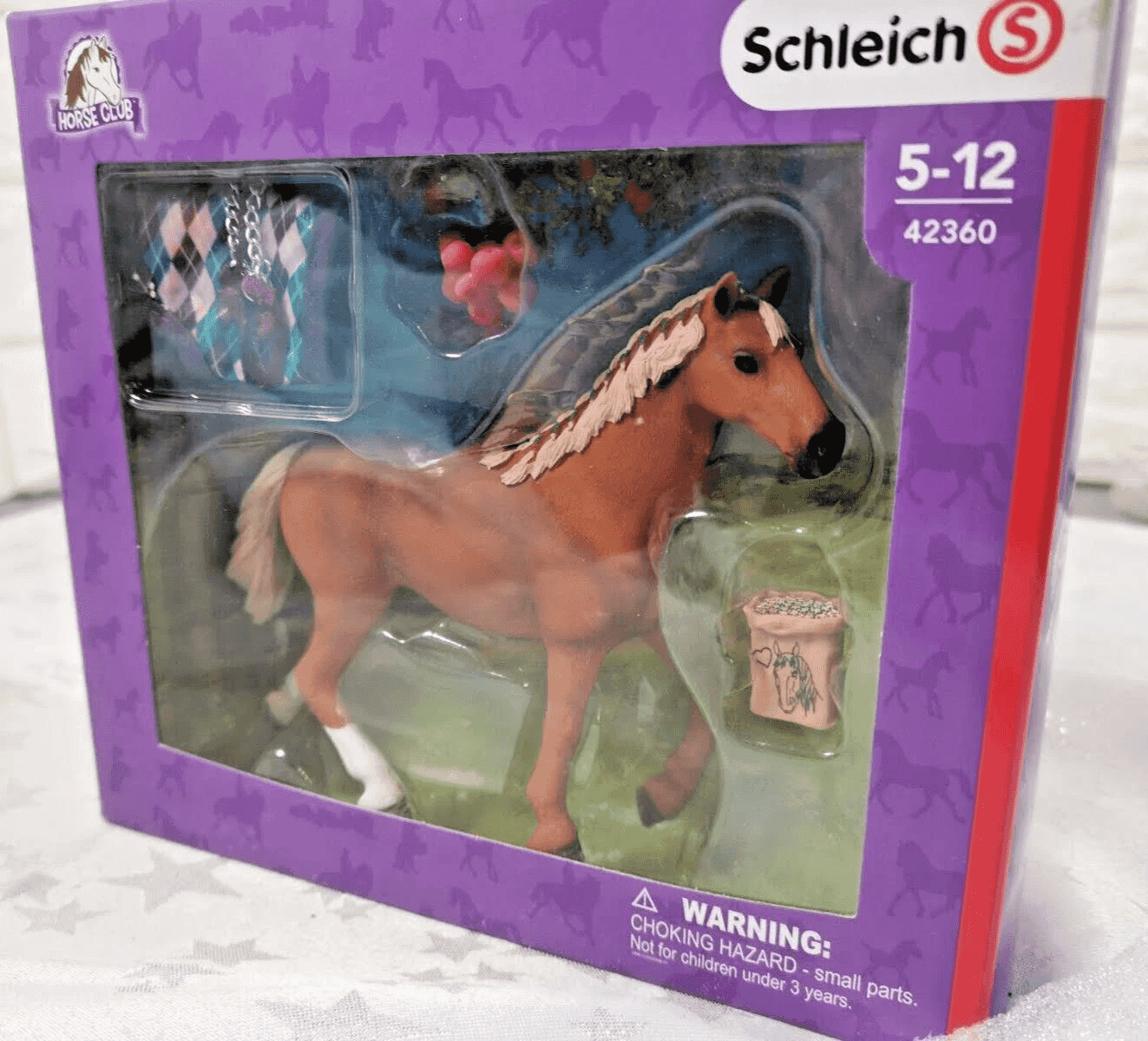 Schleich Pferdespielzeug in lila Box mit braunem Pferd, Sattelzeug und Zubehör.