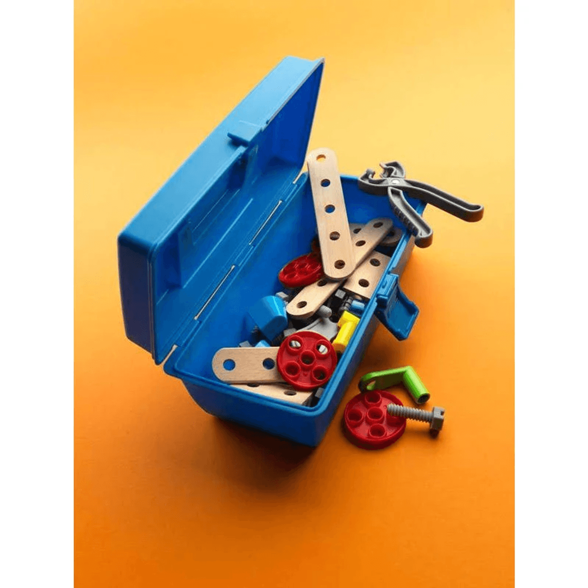 Una caja de herramientas de juguete azul abierta llena de piezas de madera coloridas, ruedas y herramientas sobre fondo naranja.
