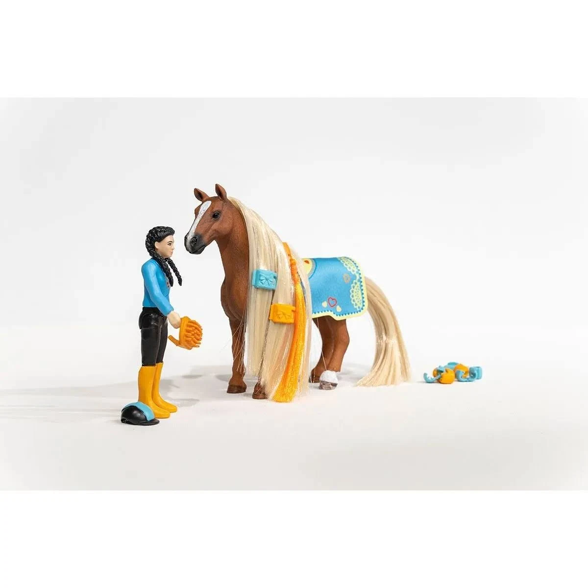 Eine Spielzeugpuppe mit blauem Oberteil und ein braunes Pferd mit langer blonder Mähne stehen auf weißem Grund.