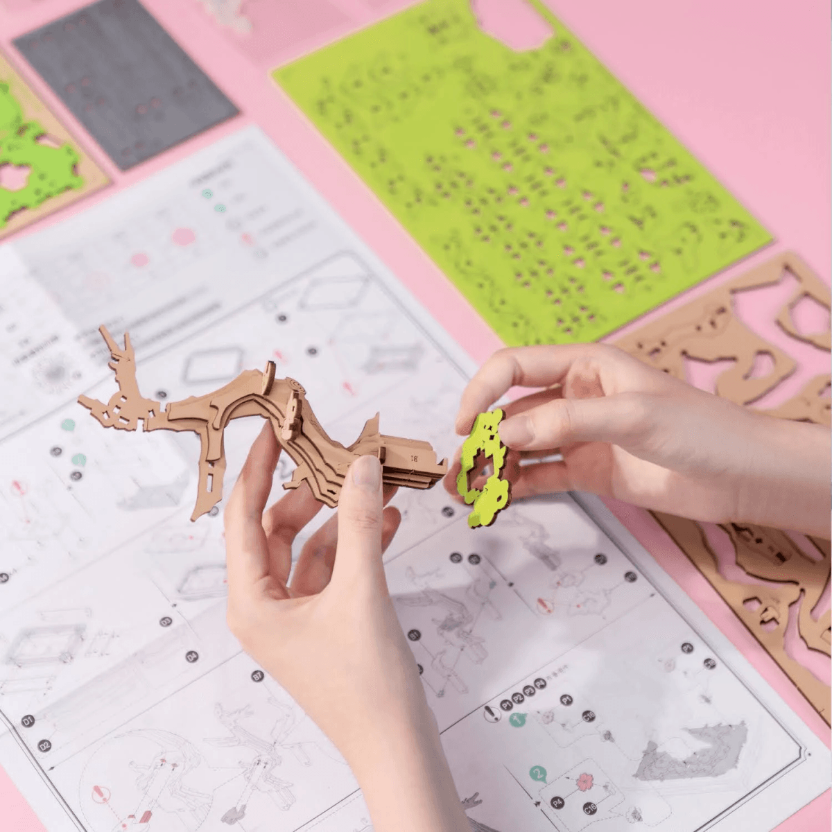 Manos ensamblan un rompecabezas 3D de madera sobre instrucciones, con piezas coloridas alrededor en una mesa rosa.