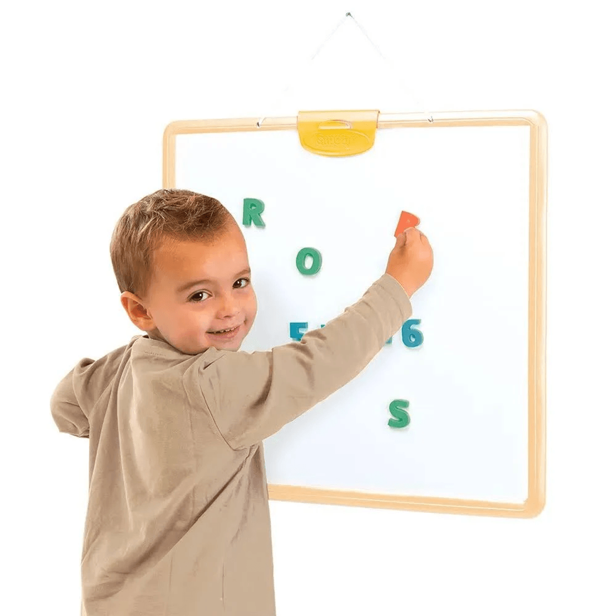 Un niño pequeño juega con letras y números magnéticos de colores en una pizarra blanca.