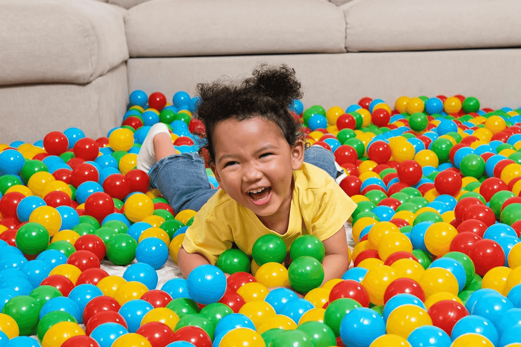 Un niño feliz con una camiseta amarilla ríe en una piscina de bolas llena de bolas coloridas azules, rojas y amarillas.