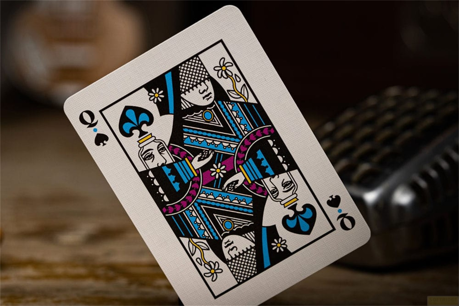 Une carte à jouer montrant la Dame de Pique en bleu, noir et blanc avec des motifs floraux.