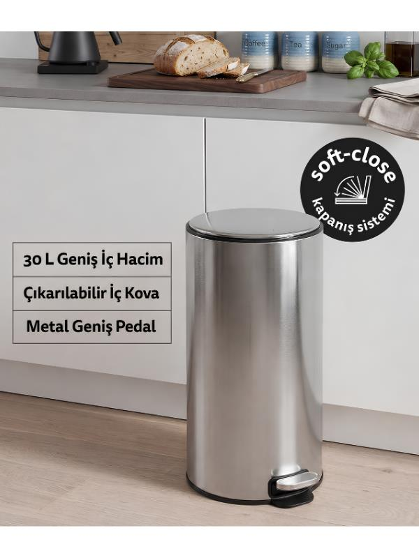 Beyaz dolaplı ve ahşap zeminli modern bir mutfakta parıl parıl parlayan metal bir pedal çöp kovası duruyor.