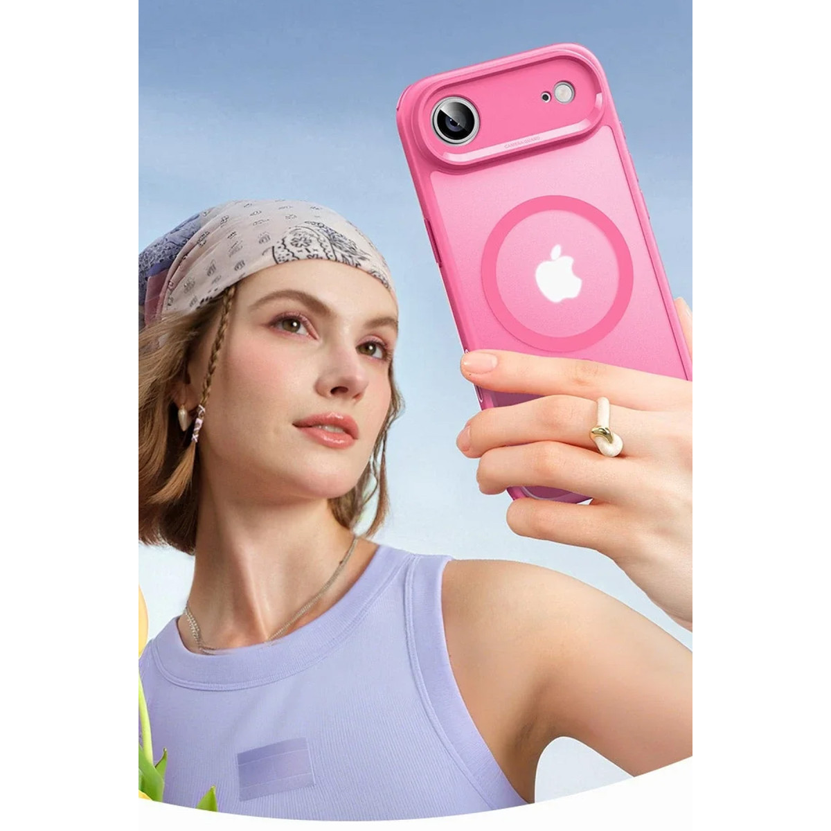 Lila üstlü ve başörtülü bir kadın pembe telefon tutarak selfie çekiyor.
