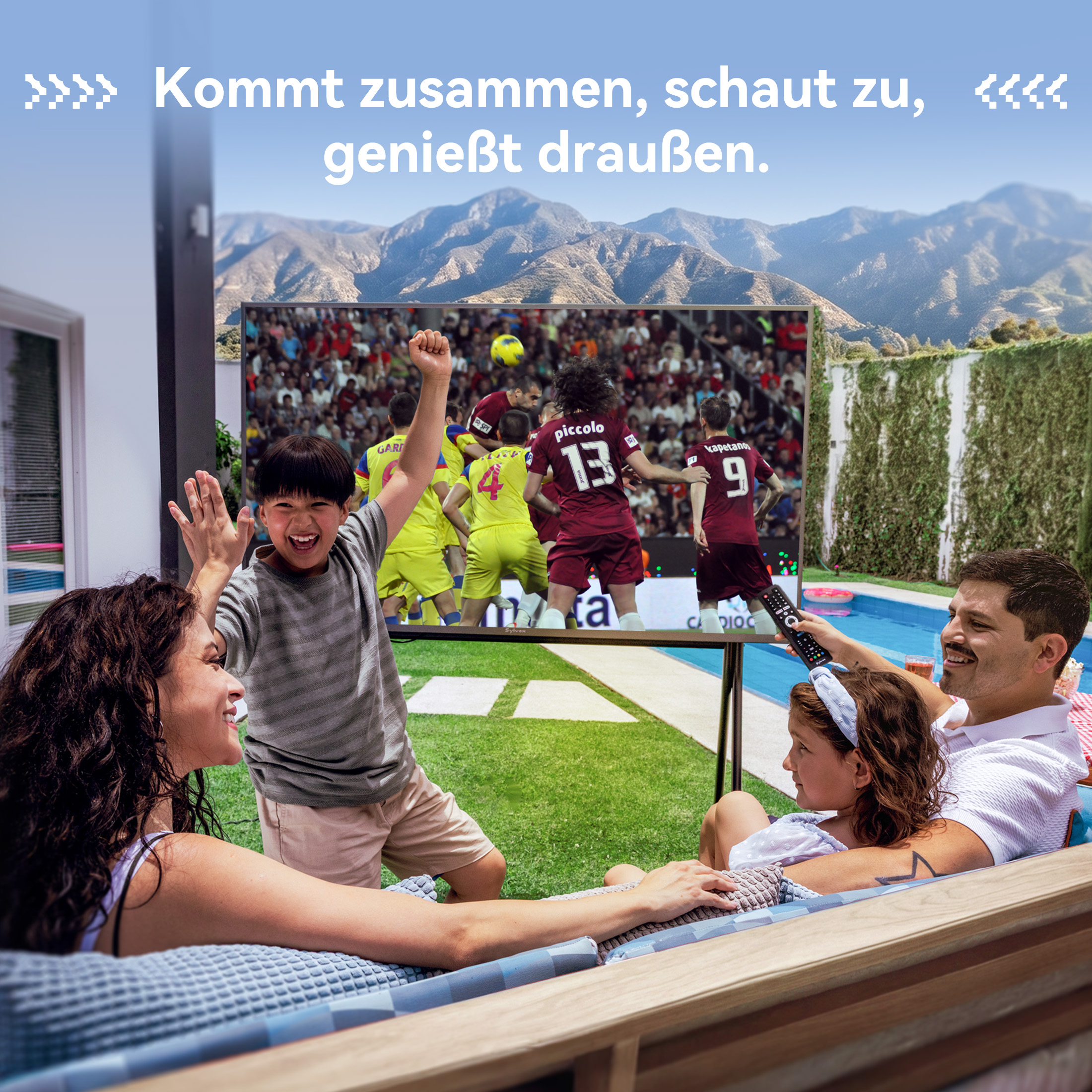 Familia viendo un partido de fútbol en un televisor exterior cerca de una piscina, con montañas y texto al fondo.