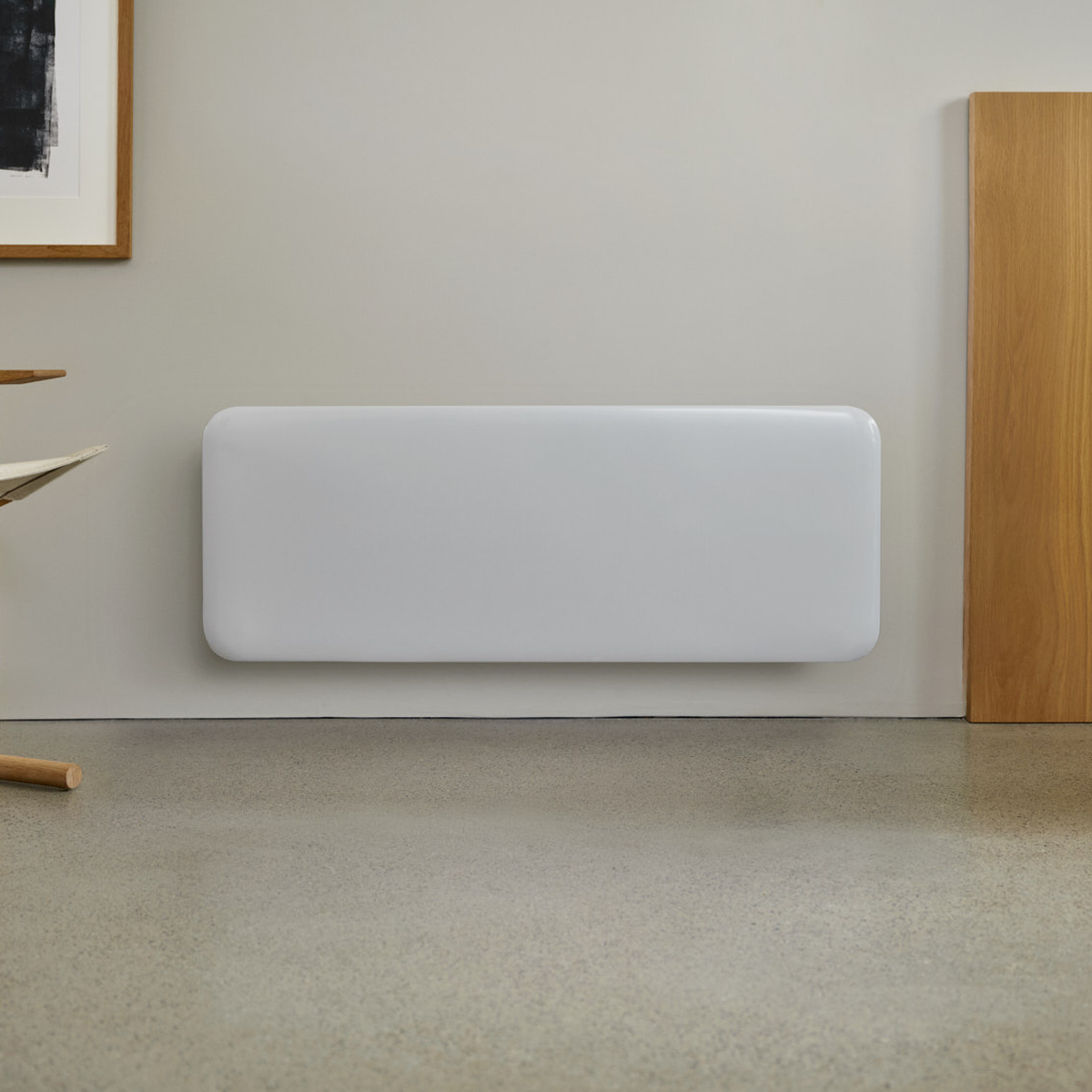 Un termosifone rettangolare bianco a parete in una stanza con pavimento in cemento, pannello di legno e quadro.