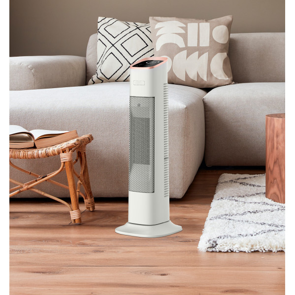 Un ventilador de torre blanco con acento cobrizo se encuentra frente a un sofá gris en la sala.