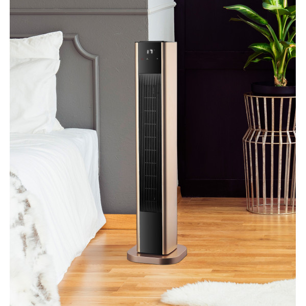 Un ventilador de torre dorado y negro se encuentra en un suelo de madera en un dormitorio.