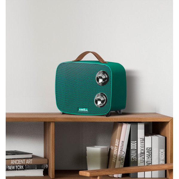 Un altavoz retro verde azulado con asa marrón y diales descansa sobre un estante de madera junto a libros.