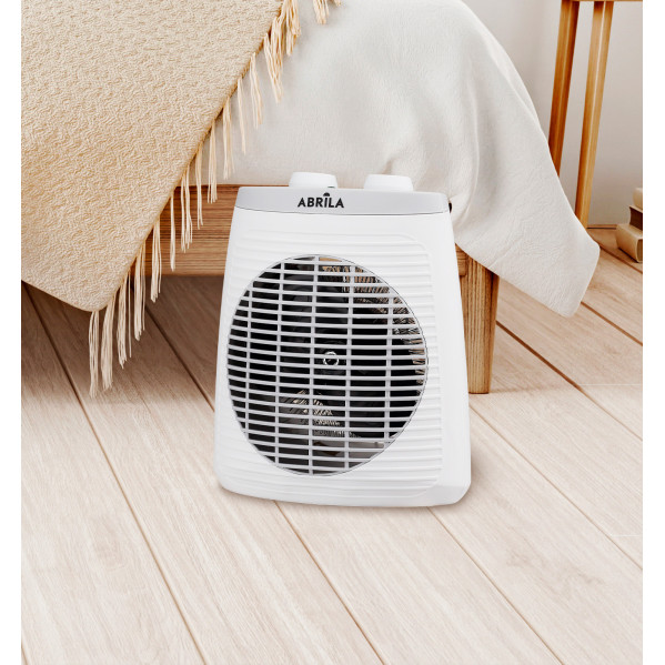 Un calefactor portátil blanco sobre suelo de madera en un dormitorio, con cama y manta de fondo.