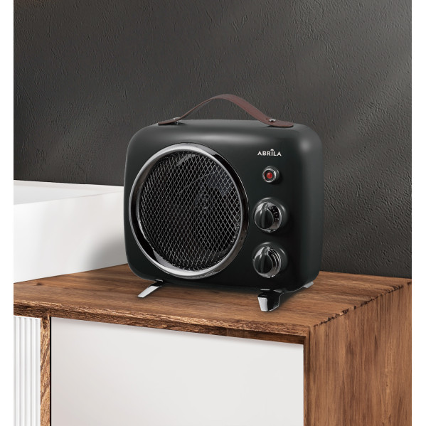 Un calefactor negro retro con asa de cuero y perillas se encuentra en un mueble de madera contra una pared oscura.