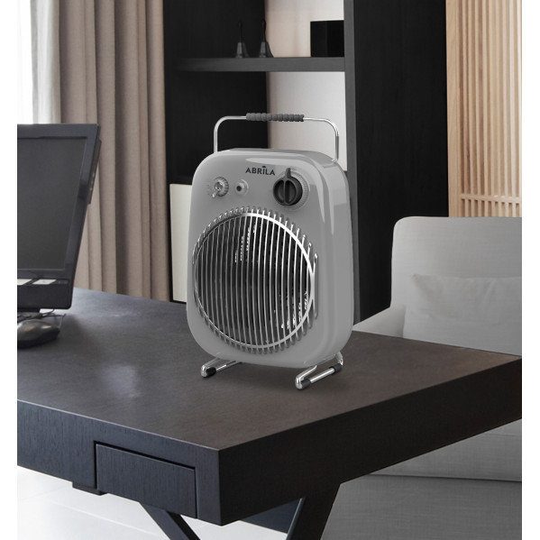 Un calefactor portátil gris con rejilla metálica está sobre un escritorio oscuro en una oficina con ordenador y sillón blanco.
