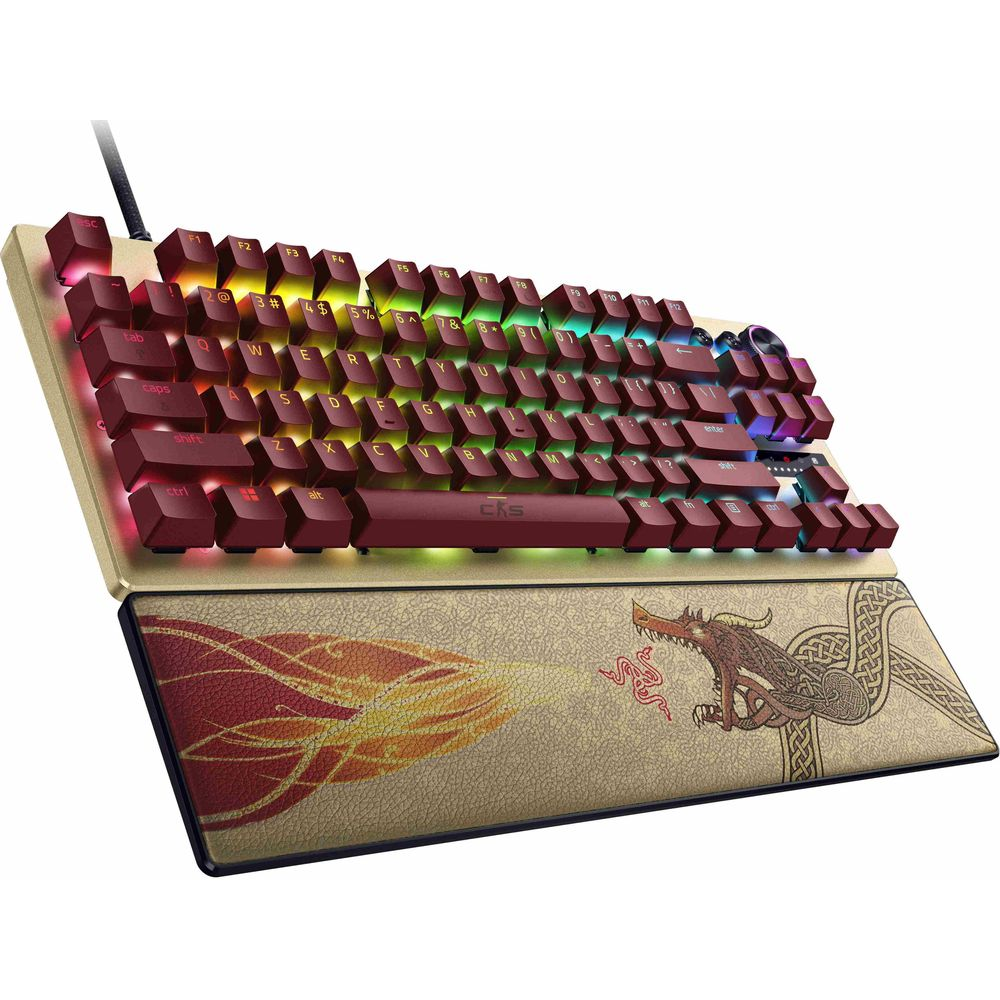 Un teclado mecánico dorado con teclas rojas, iluminación RGB y un reposamuñecas con ilustración de dragón.
