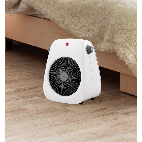 Un calefactor blanco sobre suelo de madera frente a una cama con manta mullida.
