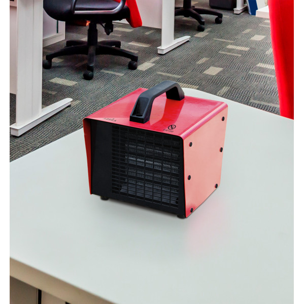 Un calefactor eléctrico rojo con asa negra está sobre un escritorio en una oficina.