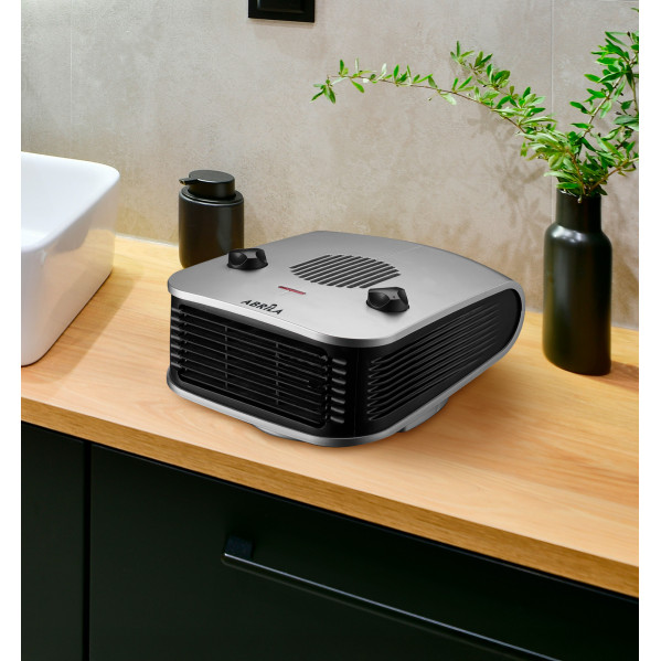 Un calefactor plateado y negro está sobre un mostrador de madera en un baño.