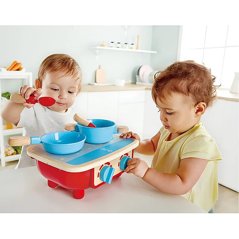 Due bambini piccoli giocano insieme con una cucina giocattolo in legno in una cucina.