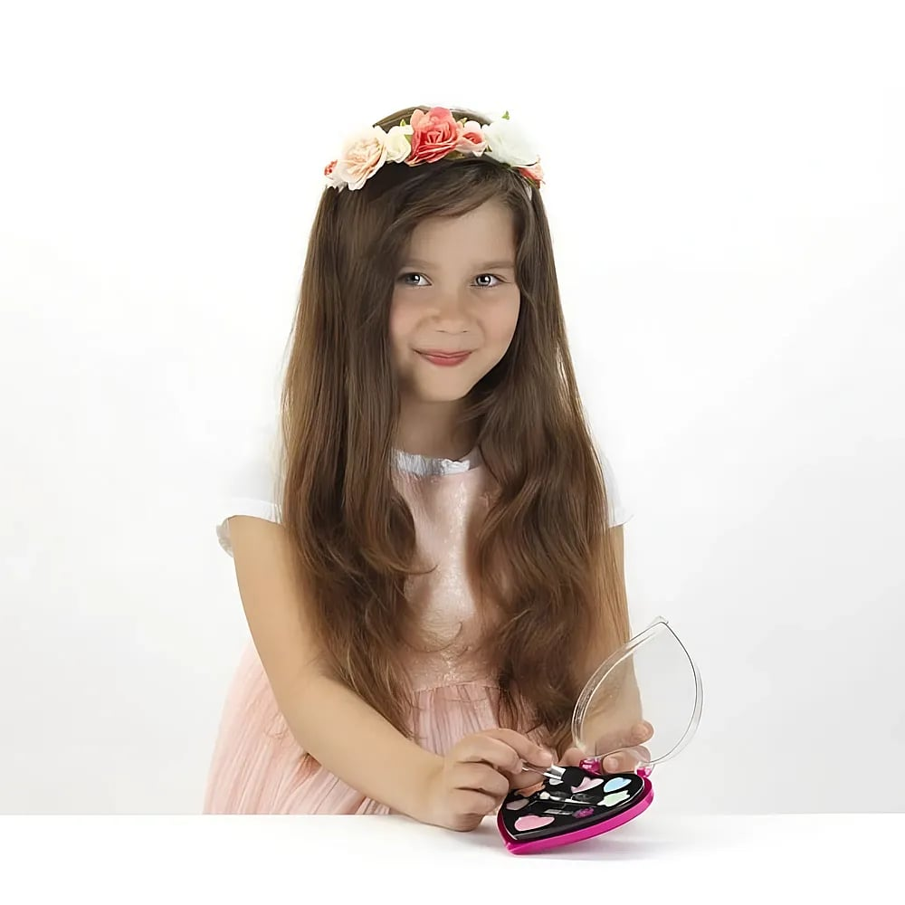 Una giovane ragazza con una corona floreale tiene un piccolo set di trucco a forma di cuore su sfondo bianco.