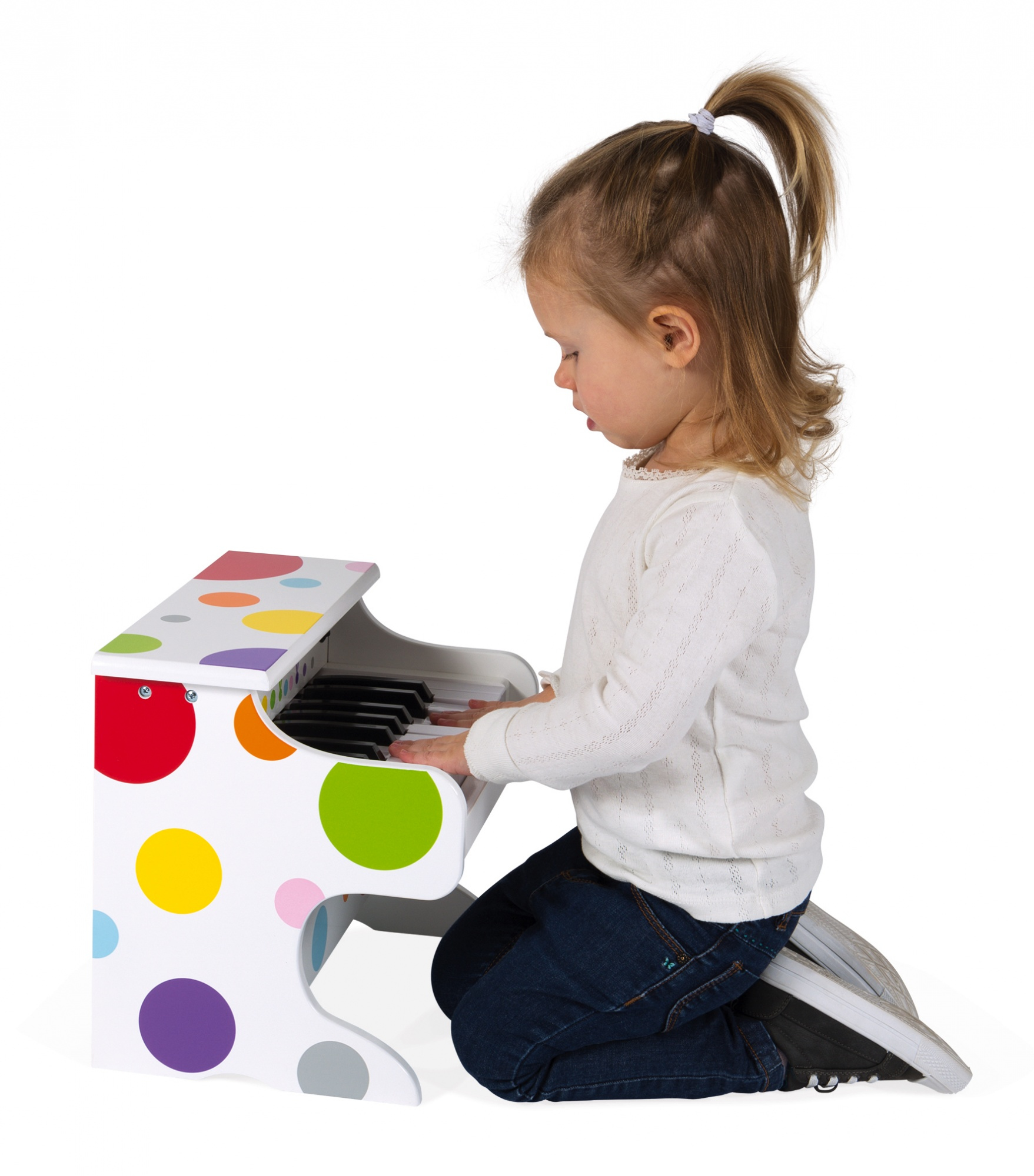 Une petite fille en haut blanc s'agenouille sur le sol et joue d'un piano jouet à pois colorés.
