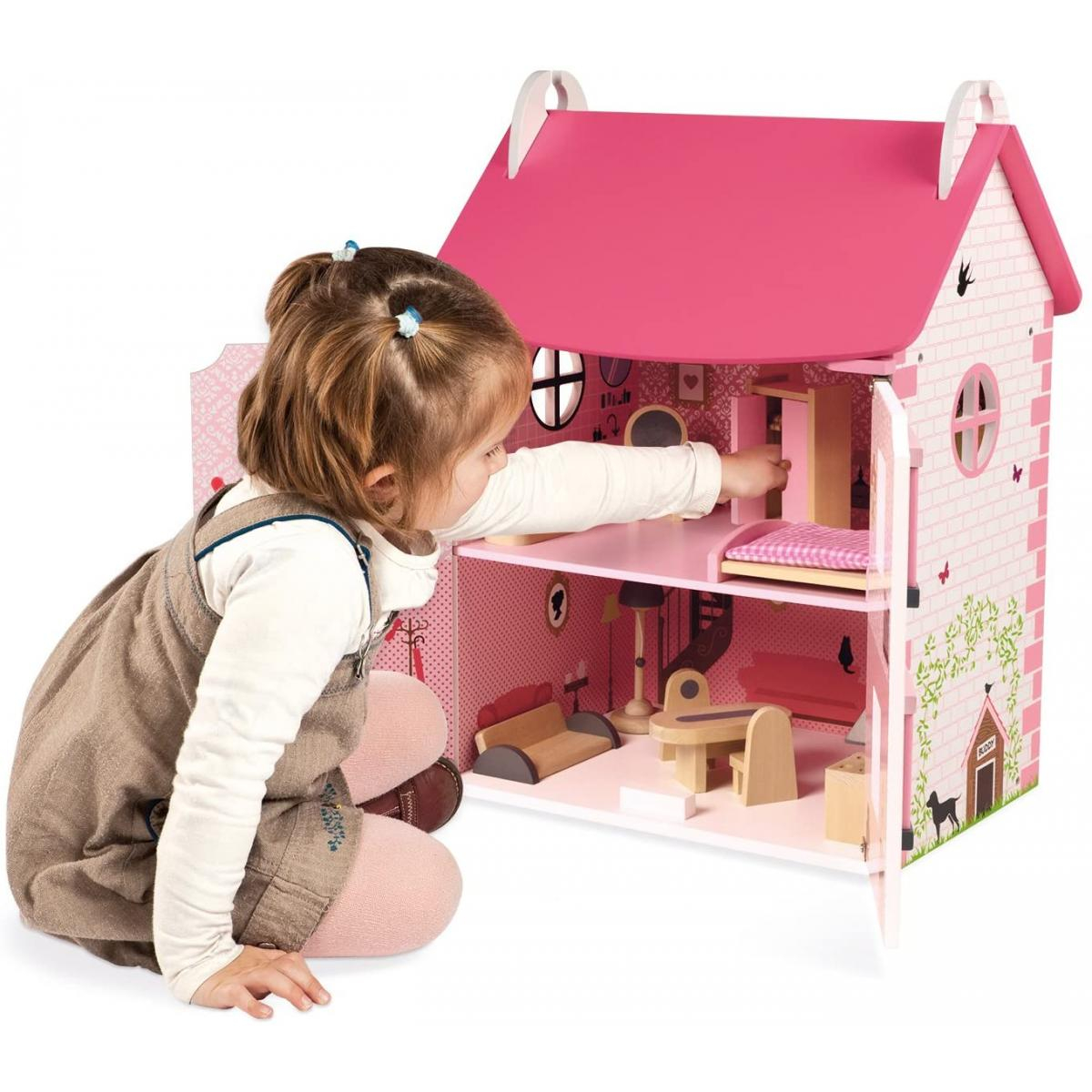 Ein junges Mädchen kniet neben einem großen, rosa-weißen Puppenhaus aus Holz und arrangiert Miniaturen.