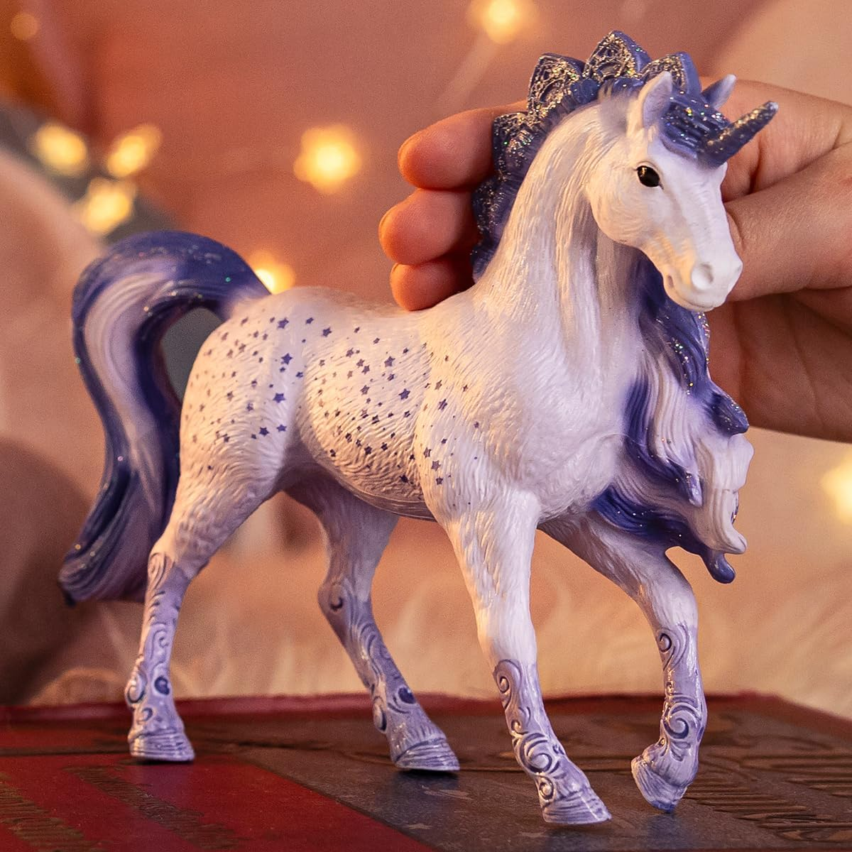 Una mano regge un unicorno bianco con criniera viola e stelle.