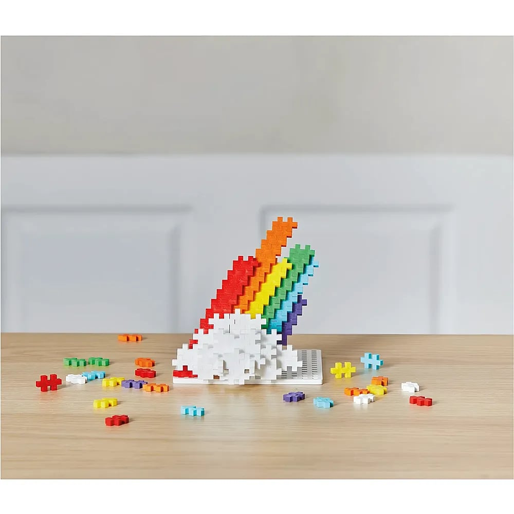Ein farbenfroher Regenbogen aus Plus-Plus-Steinen auf einer Holzoberfläche mit losen Bausteinen.