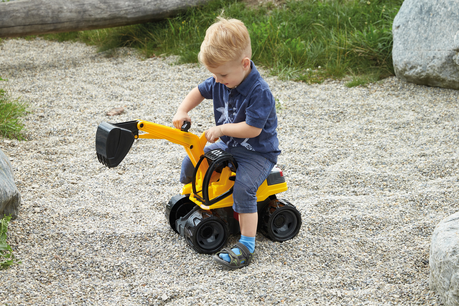 Bambino seduto su un escavatore giocattolo giallo nella ghiaia.