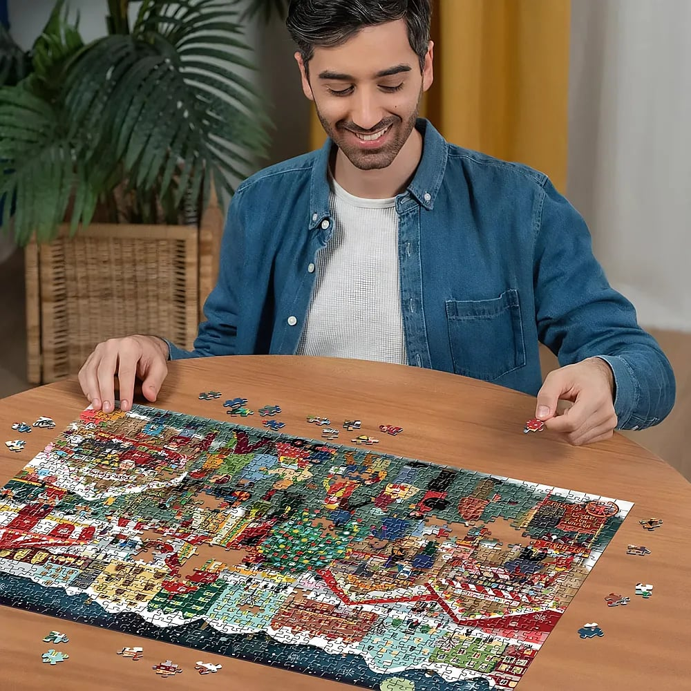 Ein lächelnder Mann sitzt an einem Holztisch und setzt ein großes Puzzle zusammen.