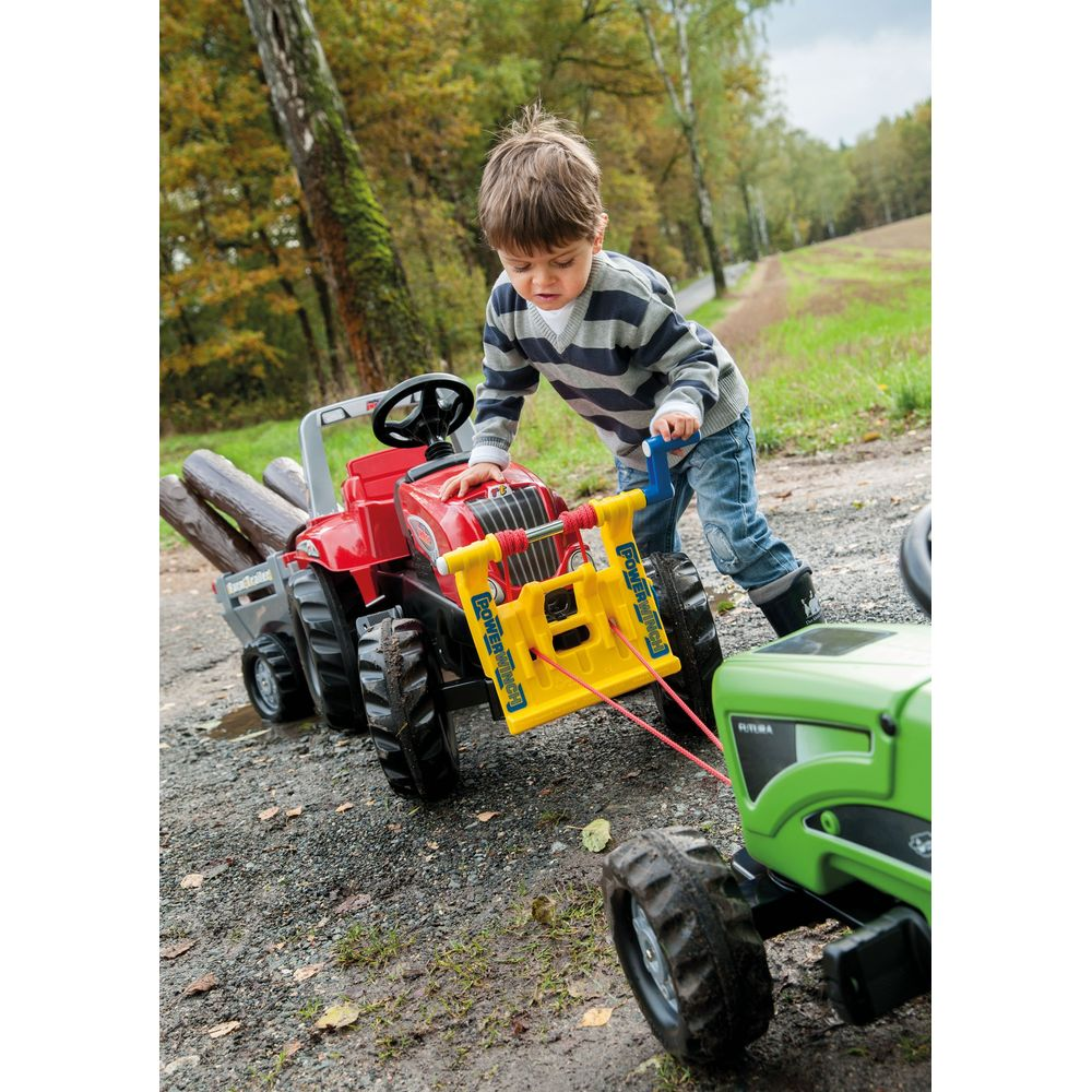 Ein kleiner Junge spielt draußen auf einem Feldweg mit einem roten Spielzeugtraktor und zieht einen grünen Spielzeugtraktor.