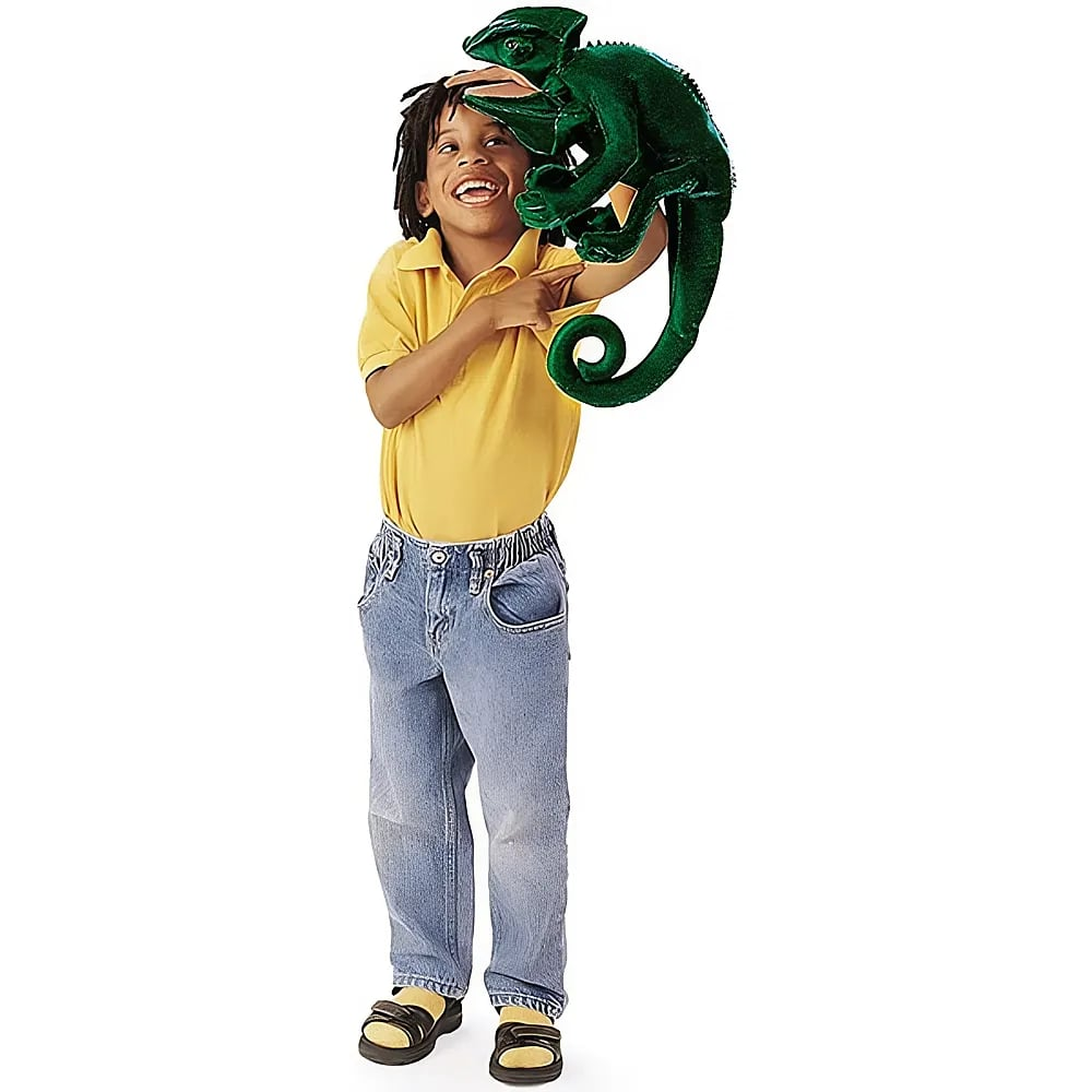 Un jeune garçon souriant portant une chemise jaune et un jean, tenant une grande marionnette caméléon verte.